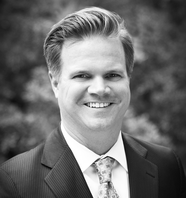 Black and white headshot of smiling man wearing a jacket and tie