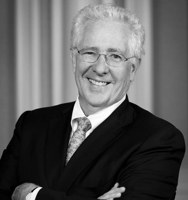 black and white headshot of smiling man wearing glasses, jacket, and tie